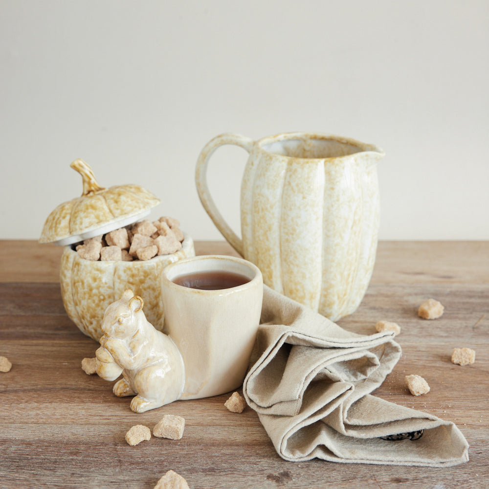 Ceramic pitcher, mug, and decorative items on a wooden surface with a neutral background.