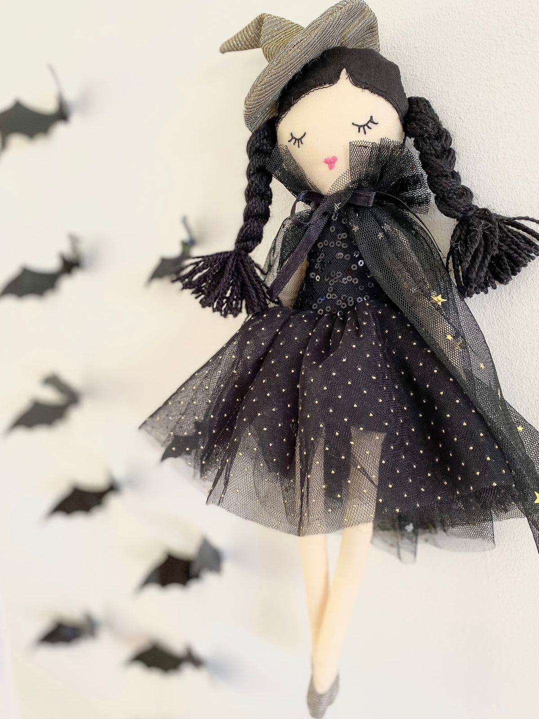 Halloween-themed doll with black dress and witch hat on a white background with black bats.
